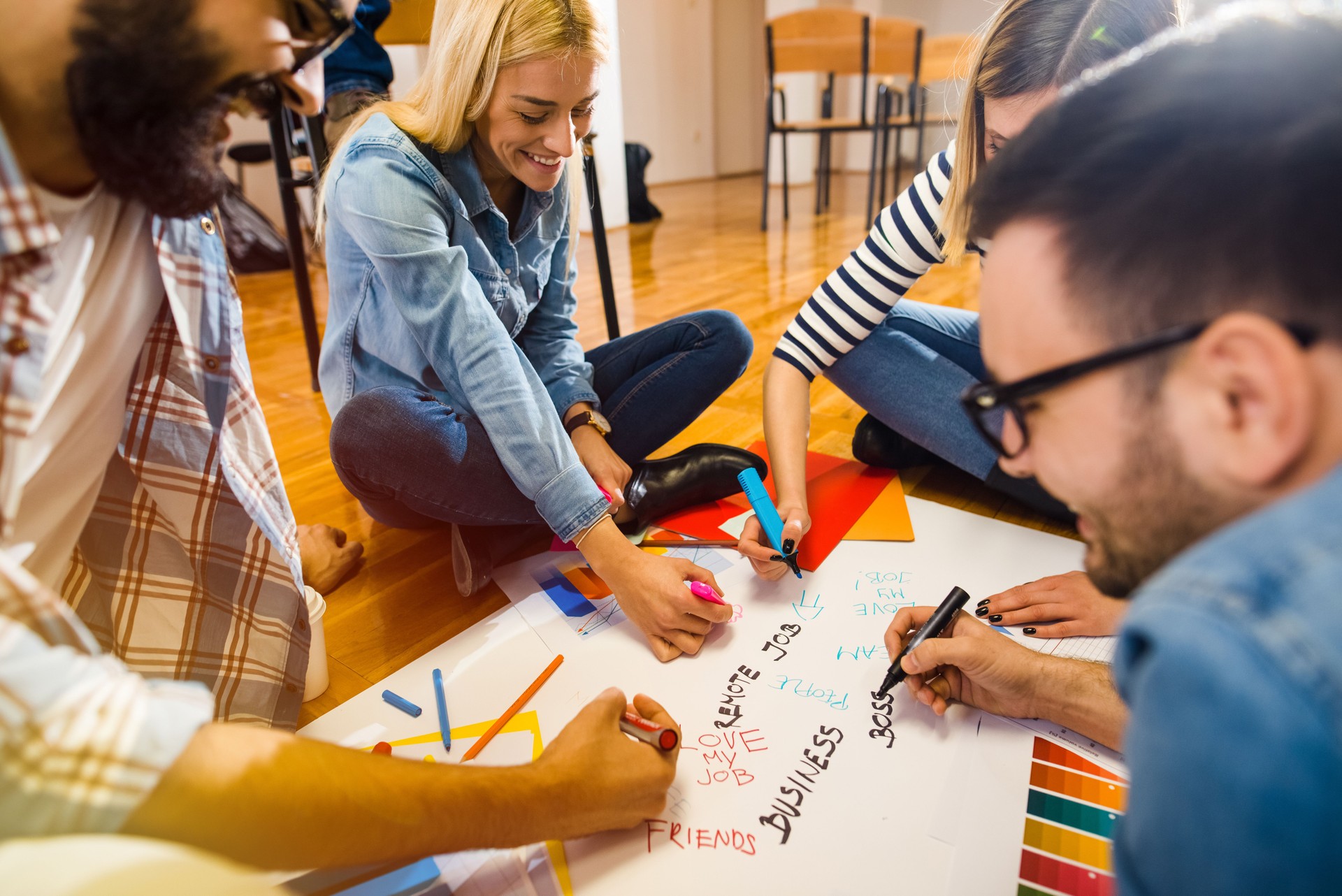 Group of young creative designers sitting on a floor and taking notes on big paper. Team work is important.